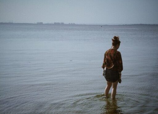 Back of woman standing in shallow waters looking down.
