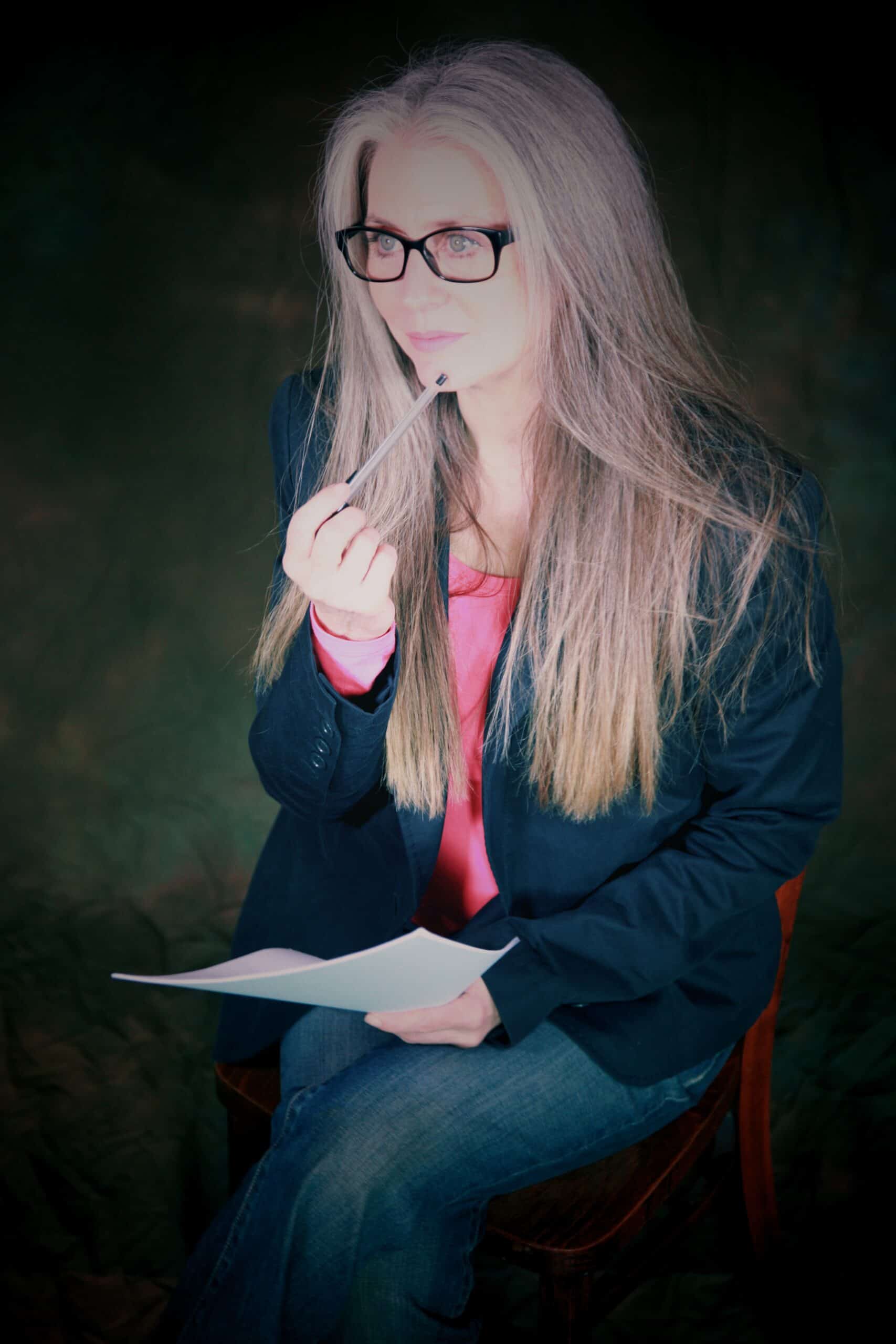 Woman hypnotherapist sitting on chair holding clip board and pen.