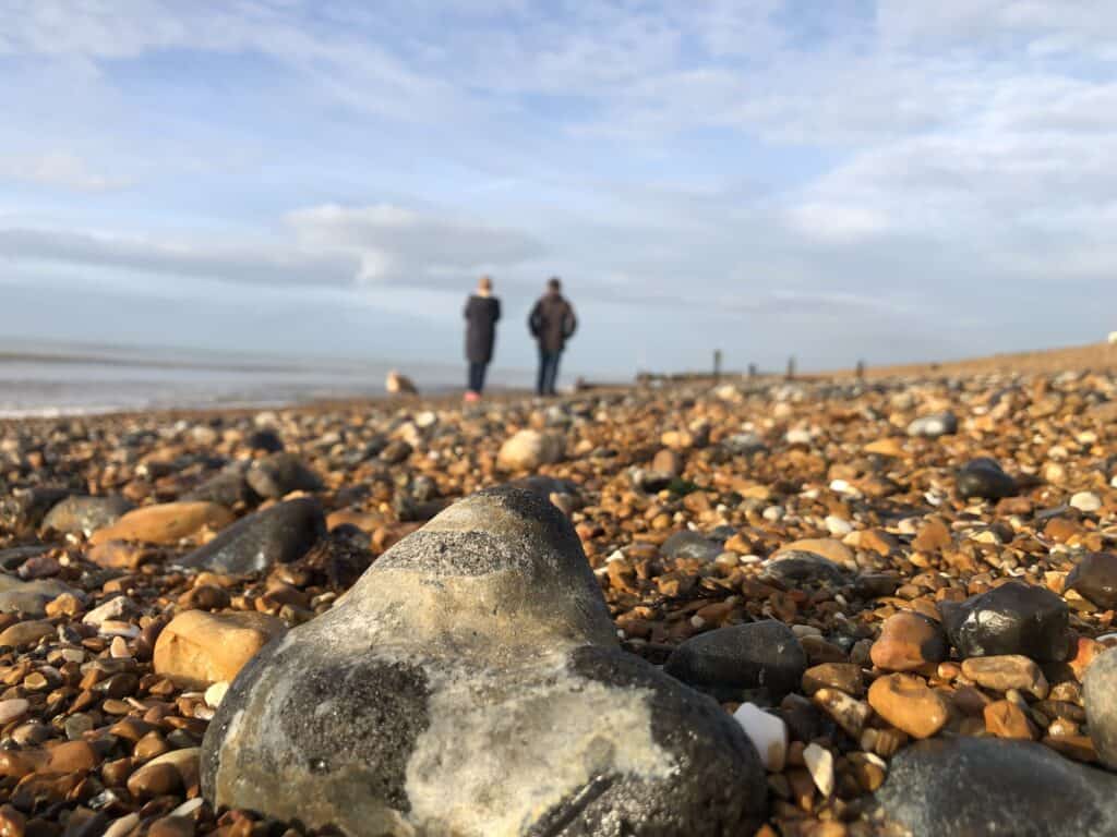 Couple on pebble beach blue sky. Phone Dependence. 