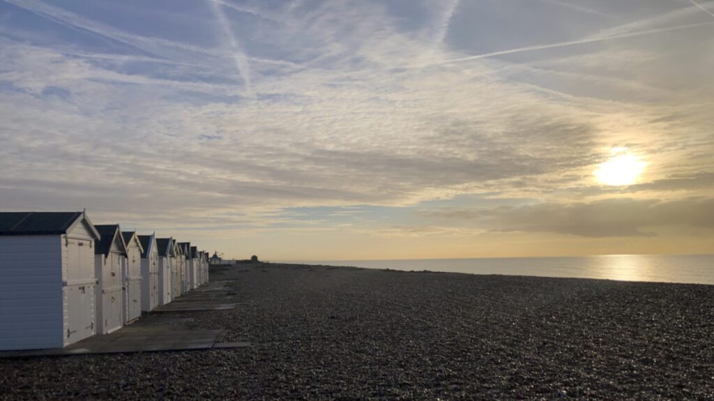 Calm coastal scene at sunset. ow of beach hut bathed in orange light from the setting sun.